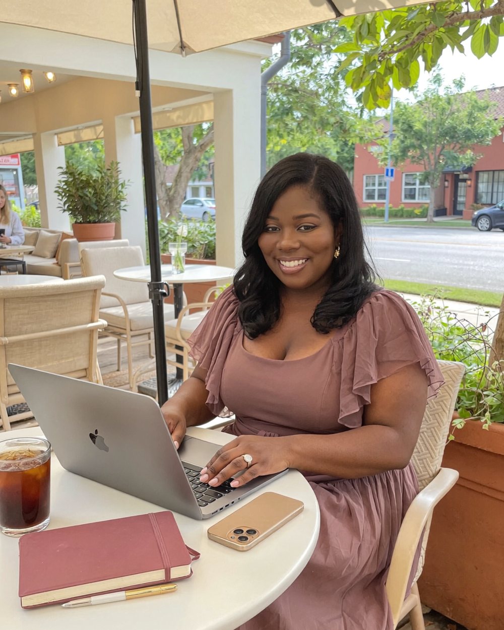 Tantanea Pernell smiling while working on a laptop at a sidewalk cafe table